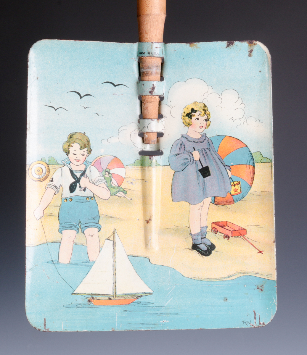 A TIN LITHO CHILD'S SAND SHOVEL WITH WOOD HANDLE