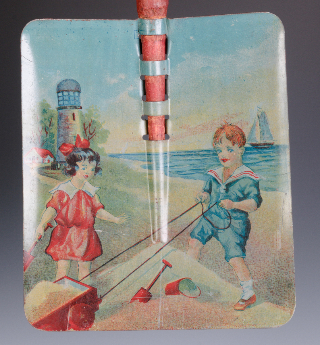 A CHILD'S TIN LITHO SAND SHOVEL WITH WOOD HANDLE